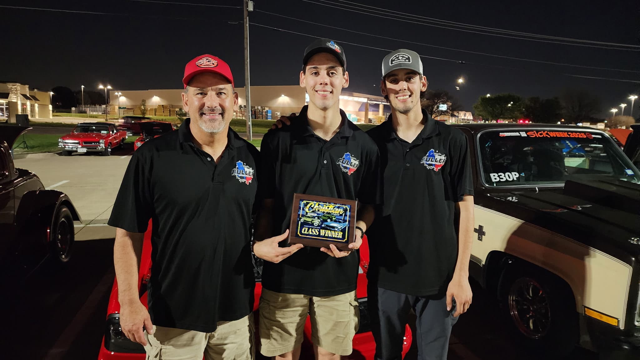 The Fuller Motor Sports team in matching shirts, holding a class winner plaque at Sick Week 2025, with their race cars behind them