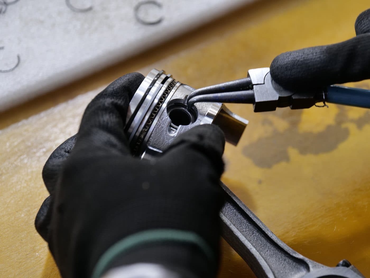 Gloved hands fitting a piston to its connecting rod on the bench